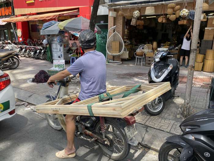 A man rides a moped with a stack of wooden window frames around his waist