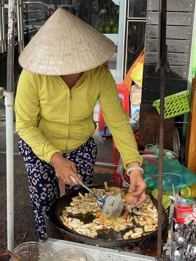 A lady in a straw hat cooks street food in a pan